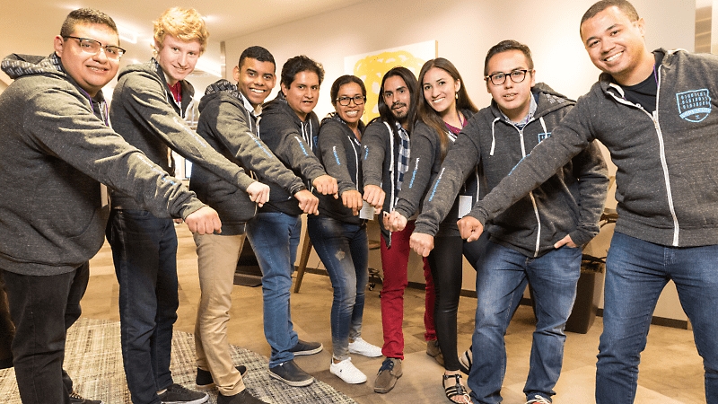 A team of coworkers standing in a semi-circle holding their fists in the center and smiling