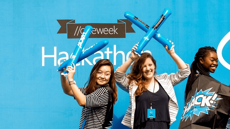 Three people smiling and posing in front of a Hackathon sign.