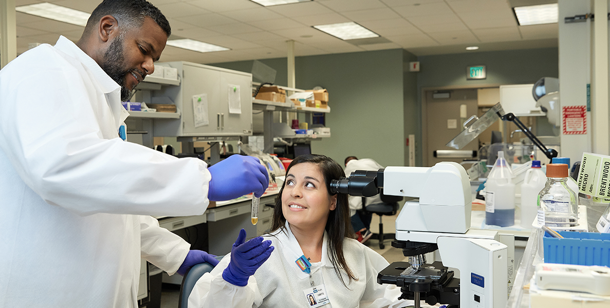 Male laboratory professional handling sample to female laboratory professional in lab setting