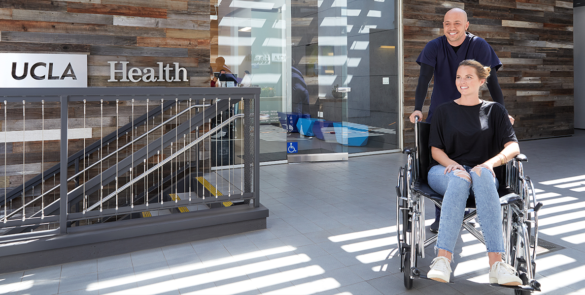 Male nurse pushing female patient in wheelchair outside of hospital