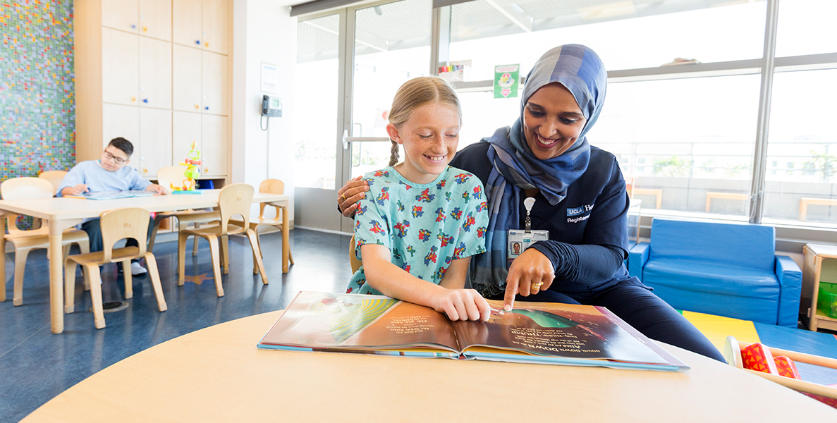 Female nurse reading story to female pediatric patient and male pediatric patient reading at table nearby