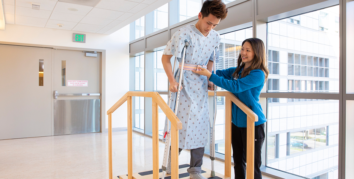 Female physician therapist helping male patient using crutches