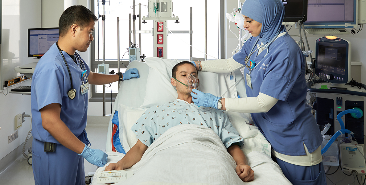 Male and female clinical professionals helping patient with oxygen at hospital bedside