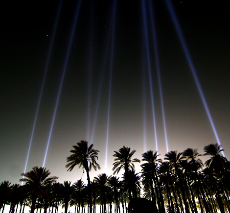 Silhouette of palm trees with searchlights shining upwards