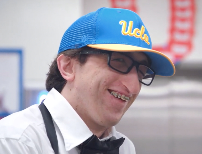 Smiling man wearing UCLA ball cap video opens in modal window