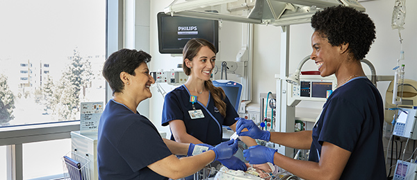 Three smiling female nurses caring for newborn in hospital labor & delivery room