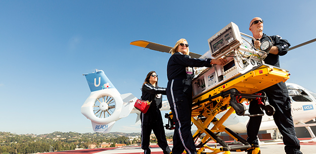 Male and female EMTs pushing critical care equipment cart on helipad