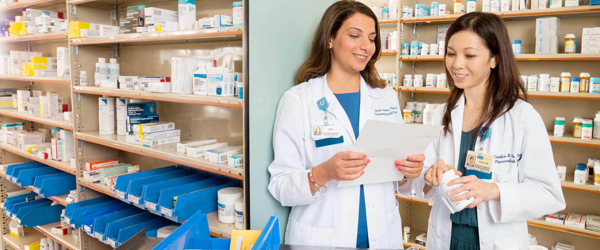 Two female pharmacists reviewing document in front of shelves of medications