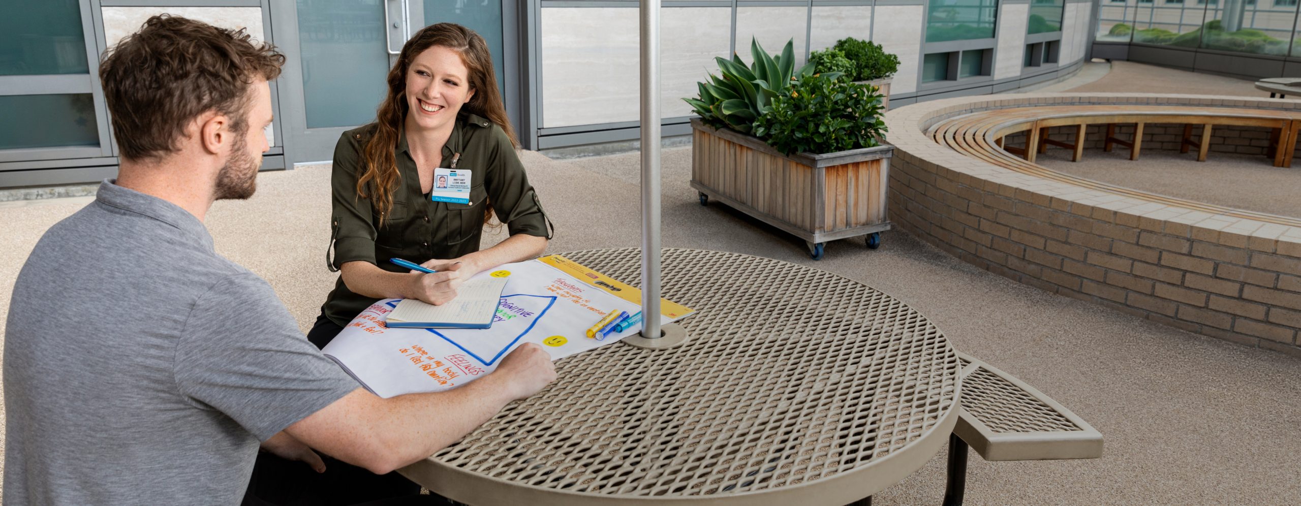 A smiling female UCLA Health onboarding expert meeting with a male new hire at a table in an outdoor setting