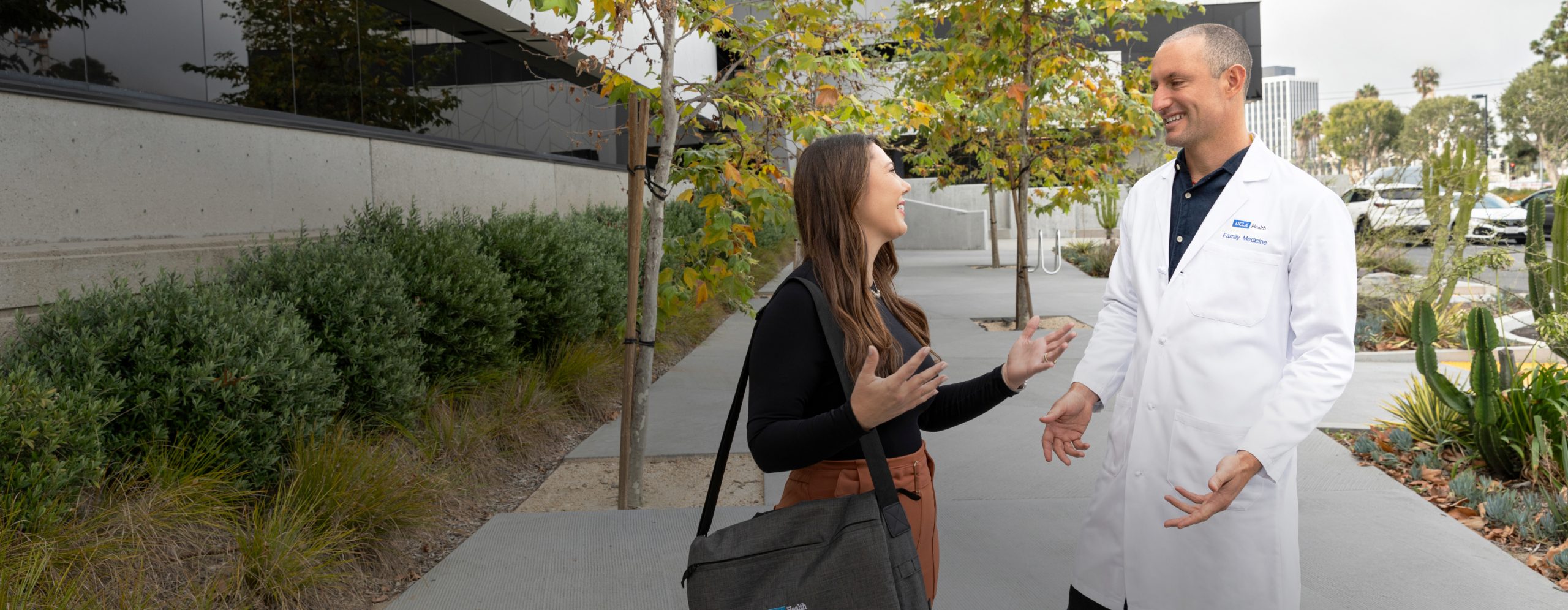 A male UCLA Health physician and a female UCLA Health business professional enjoying a conversation outside of a UCLA Health hospital