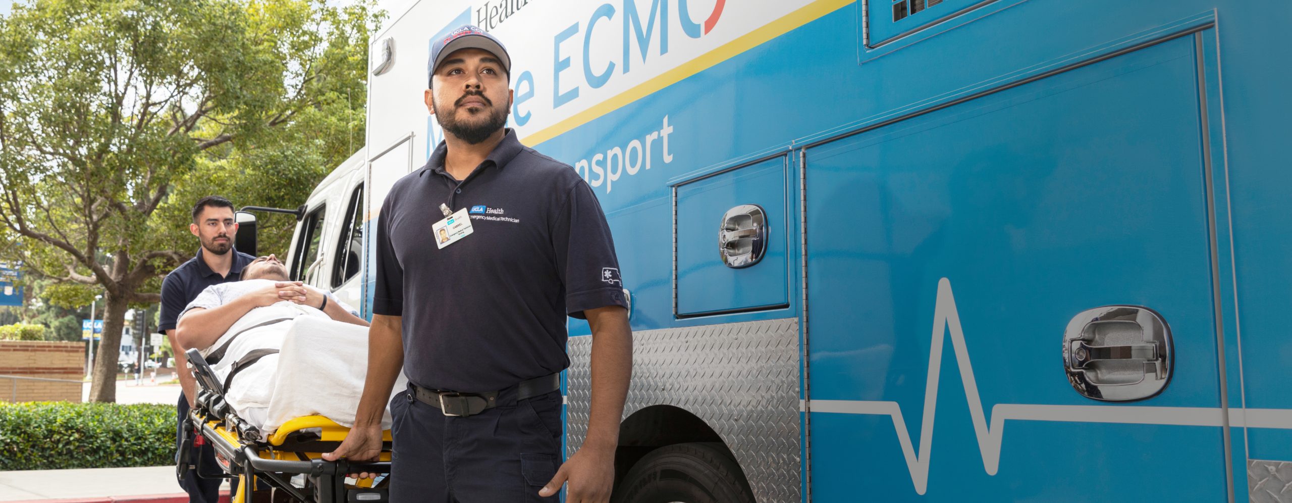 Two UCLA Health patient transport professionals moving a patient on a gurney in front of a patient transport van