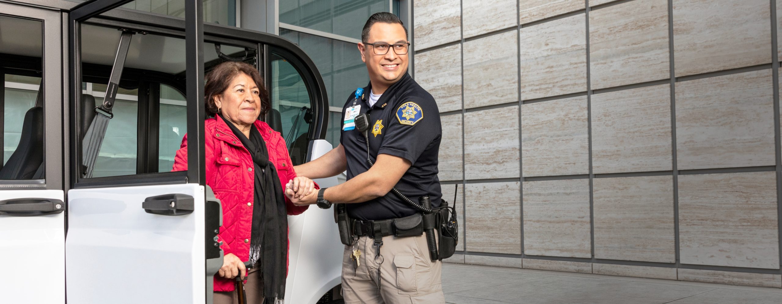 A UCLA Health security professional helping a female patient exit a vehicle