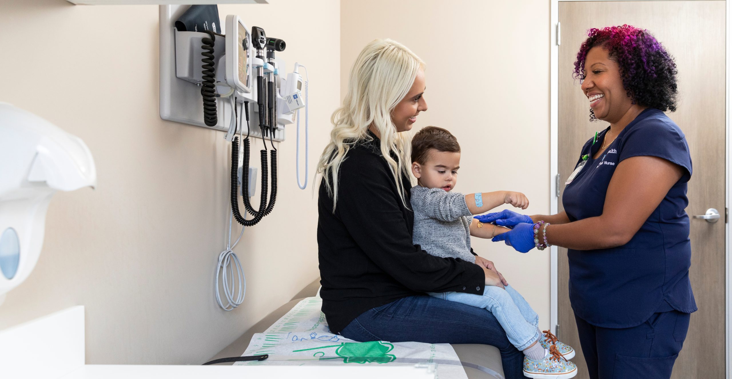 A female UCLA Health nurse engaging with a pediatric patient and his mother in an examination room