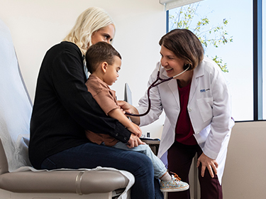 A female UCLA Health physician and a female UCLA Health nurse helping a patient in an examination room