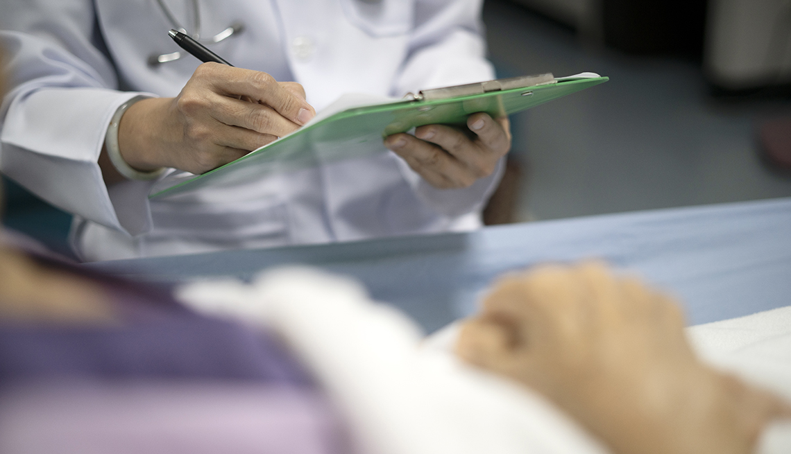 Midsection of doctor visiting patient lying down on bed at the hospital and writing on a clipboard for check up.