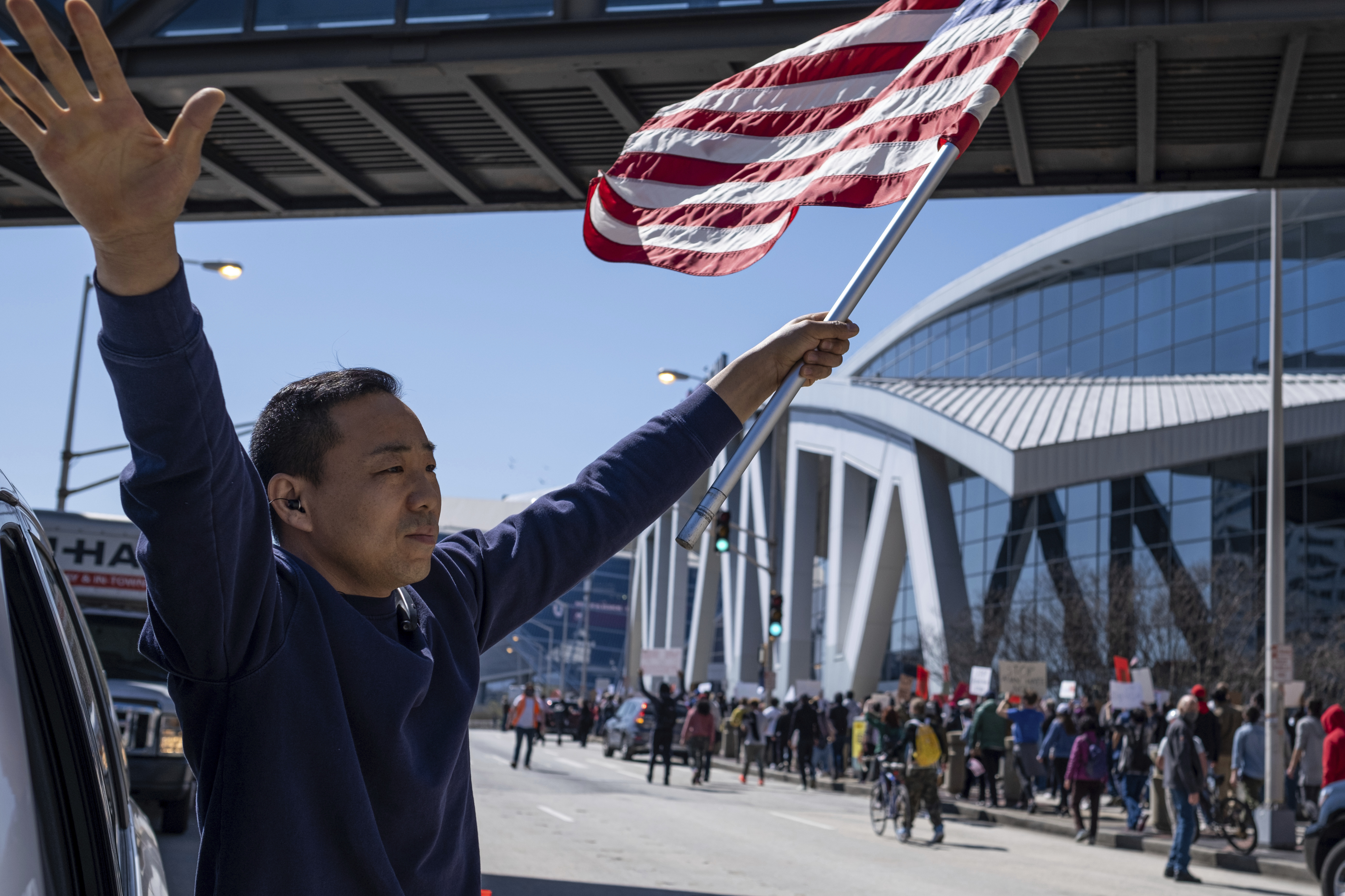 Hailun Song waves a U.S. flag and cheers marchers as a "stop Asian hate" rally in downtown Atlanta passes by Saturday afternoon, March 20, 2021.