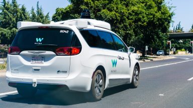 A Waymo-branded minivan prowls suburban streets.