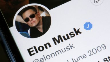 Photo illustration shows Elon Musk's Twitter profile on a phone screen, with a large Twitter logo in the background.