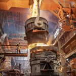 Steelworker starting molten steel pour in steelworks facility.