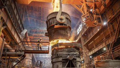 Steelworker starting molten steel pour in steelworks facility.