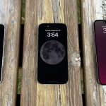 Three iPhones on a wooden picnic bench. One of them has a black screen, while the other two have always-on displays.