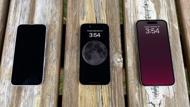 Three iPhones on a wooden picnic bench. One of them has a black screen, while the other two have always-on displays.