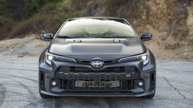 A dark grey Toyota GR Corolla seen head-on. It has a very large front grille and many air intakes and flared arches