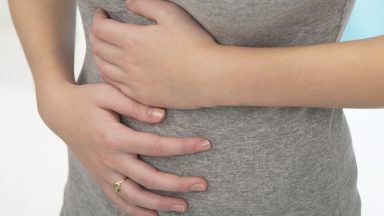 A woman experiencing abdominal pain by covering both hands over her stomach.