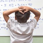 Image of a student standing before a whiteboard filled with equations.