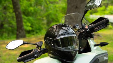 A black motorcycle helmet rests on the seat of an electric motorcycle in the woods