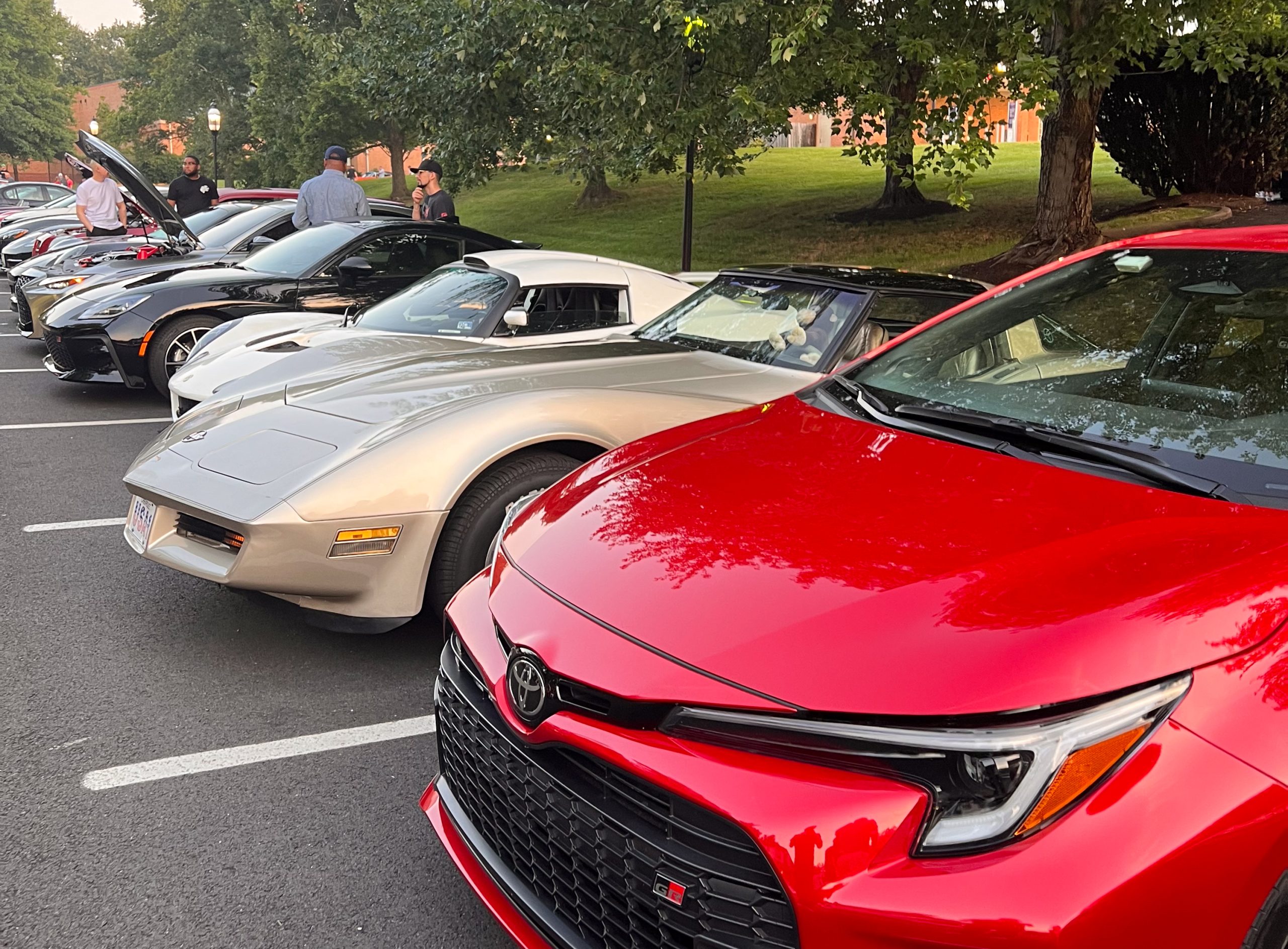 A Toyota GR Corolla parked at Cars and Coffee alongside a C3 Corvette, a Lotus Exile, A Nissan Z, A BMW M4, and some other enthusiast cars