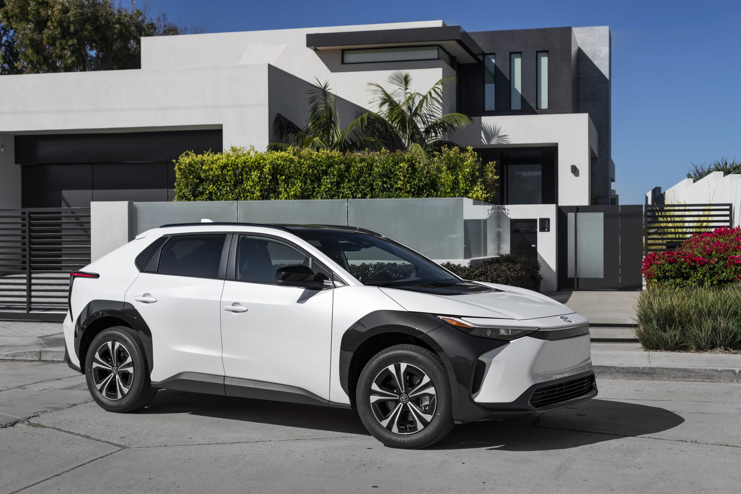 A black and white Toyota bZ4x parked in front of a modern house