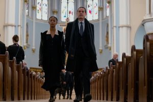 young woman and middle aged man in funeral attire walking down the aisle of a church