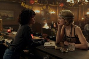 dark haired woman and blonde woman in flapper costume chatting at a bar