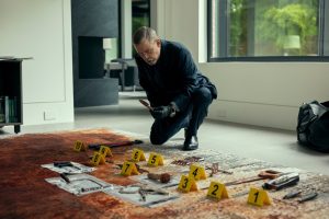 bearded older man kneeling before a series of photos and other artifacts laid out on the floor