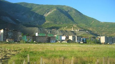 Image of apartment buildings with mine tailings behind them, and green hills behind those.