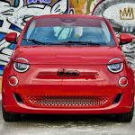 A head-on shot of a red Fiat 500e in front of a mural