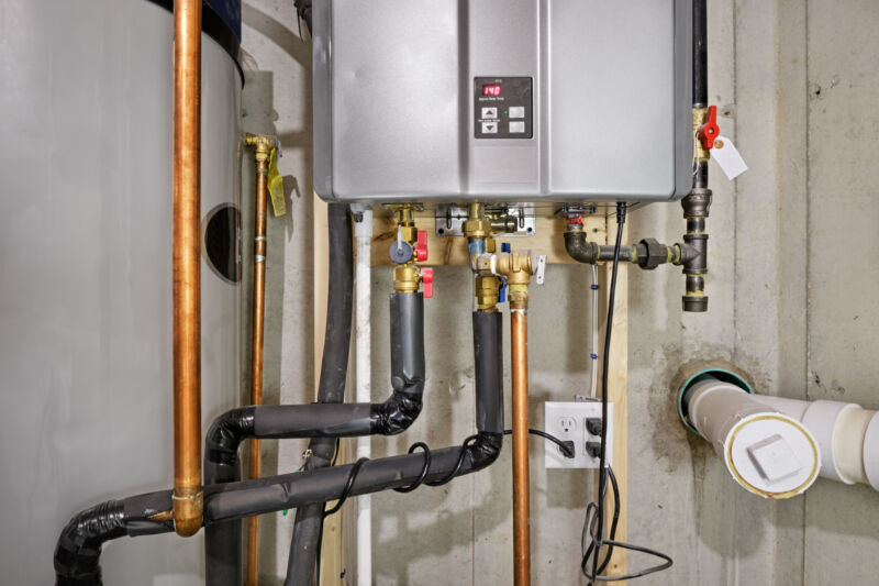 The bottom half of a tankless water heater, with lots of pipes connected, in a tight space