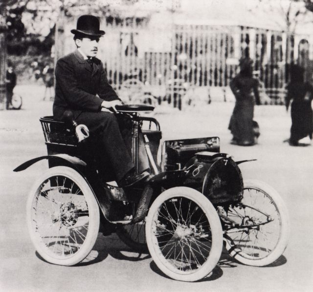 A black and white photograph of a man sitting in a Renault voiturette