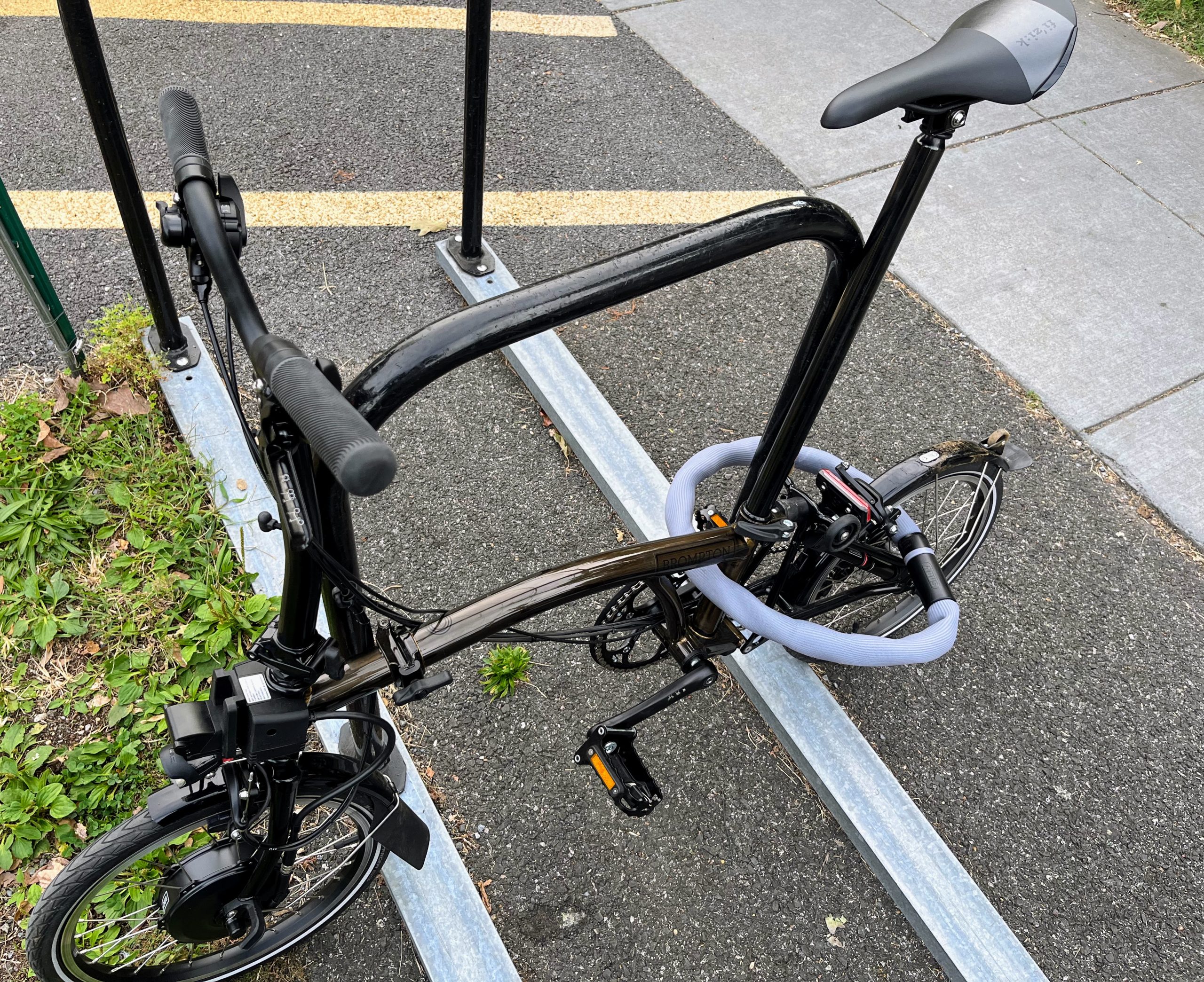 Brompton locked up loosely to post with purple chain lock.