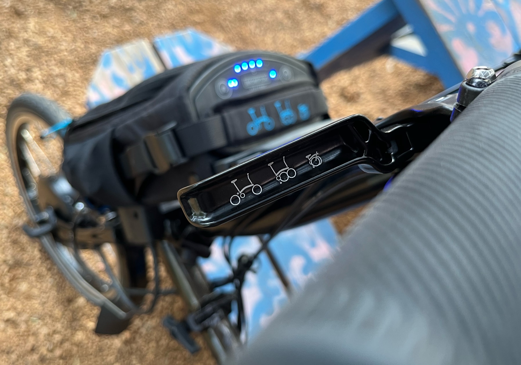 Brompton folding e-bike with its battery in the background, and a brake lever in foreground, showing a three-step fold illustration.