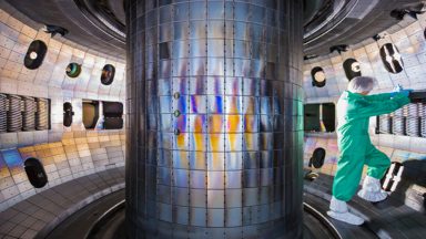 image of a person in protective clothing, standing in a circular area with lots of mirrored metal panels.