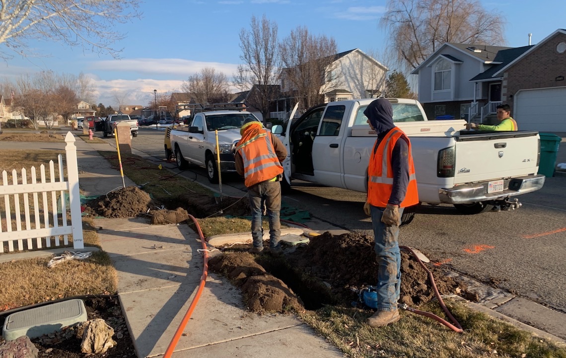 Two workmen next to a hole in which they'll be installing fiber Internet lines.