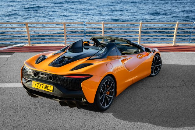 An orange McLaren Artura Spider parked by the water