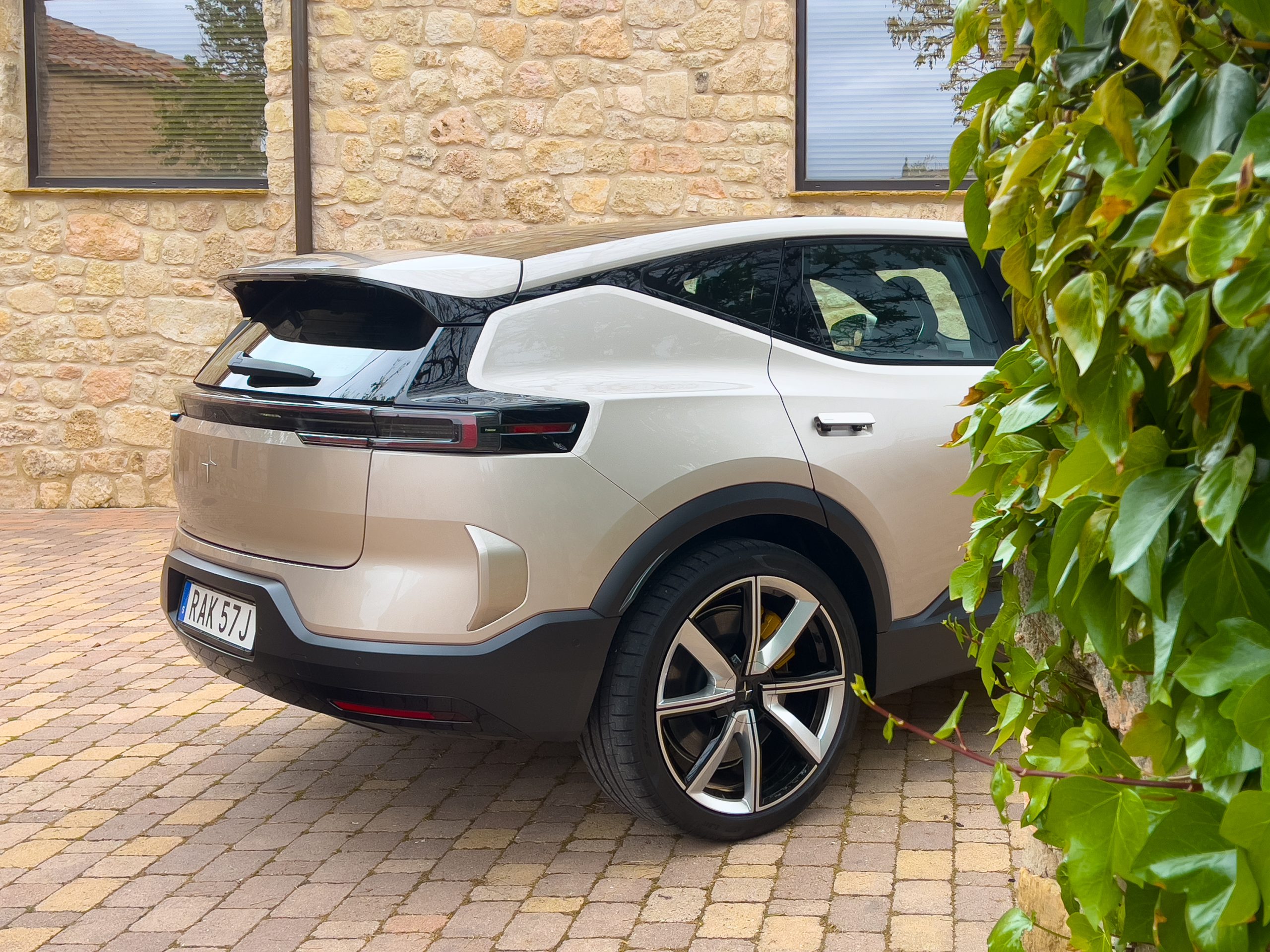 the rear half of a Polestar 3, hiding behind a stone building