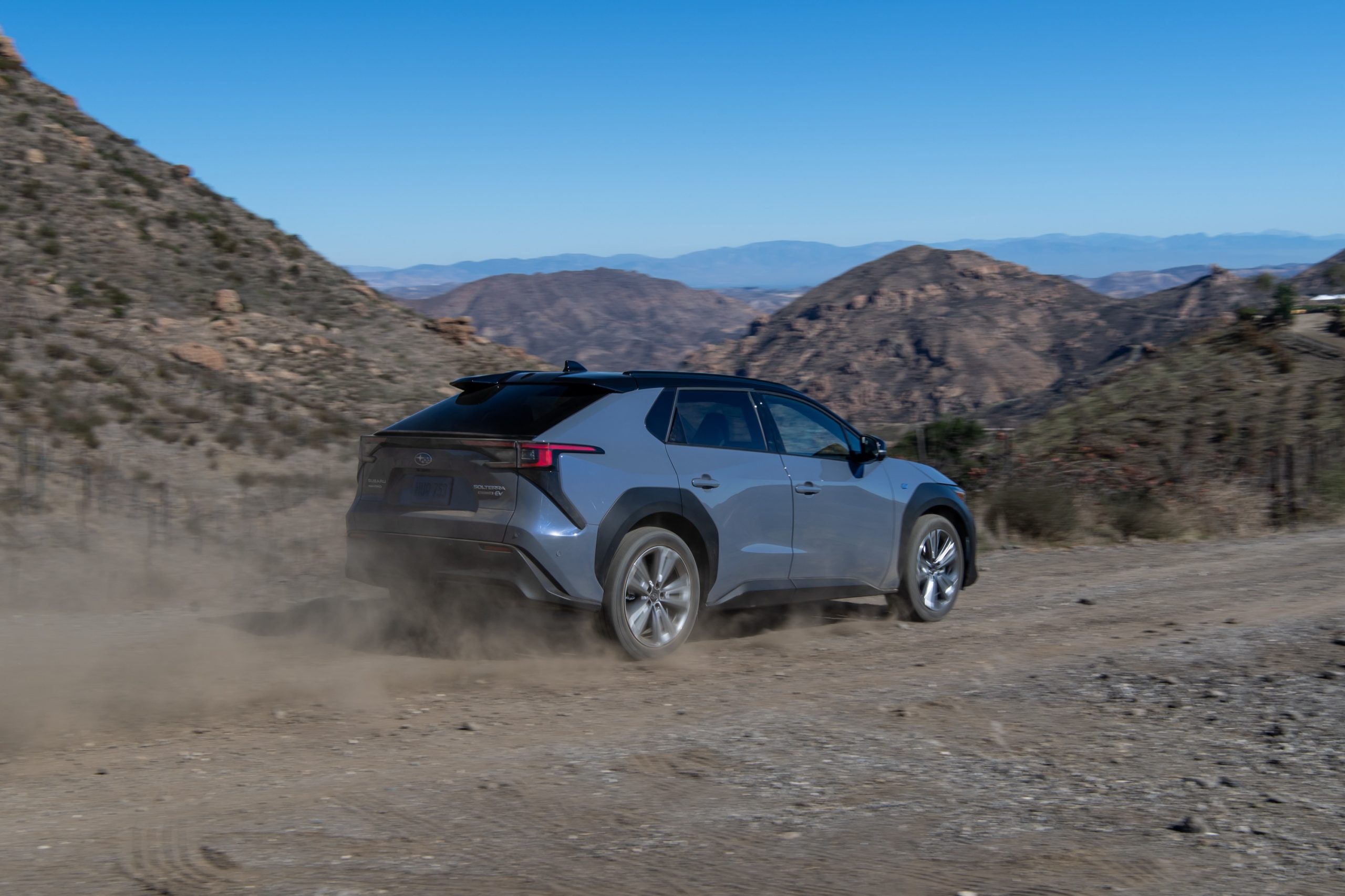 A Subaru drives away from the camera on a dirt road