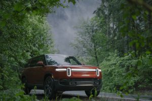 A red Rivian peeks out from some trees in the forest