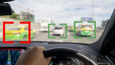 Image out the windshield of a car, with other vehicles highlighted by computer-generated brackets.