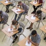 Overhead view of a classroom full of students at desks, focused on writing on papers.