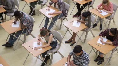 Overhead view of a classroom full of students at desks, focused on writing on papers.